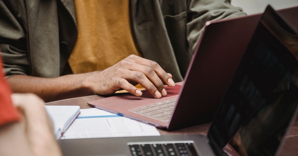 Crop unrecognizable young African American male entrepreneur in casual clothes typing on laptop while working on project in office with colleague